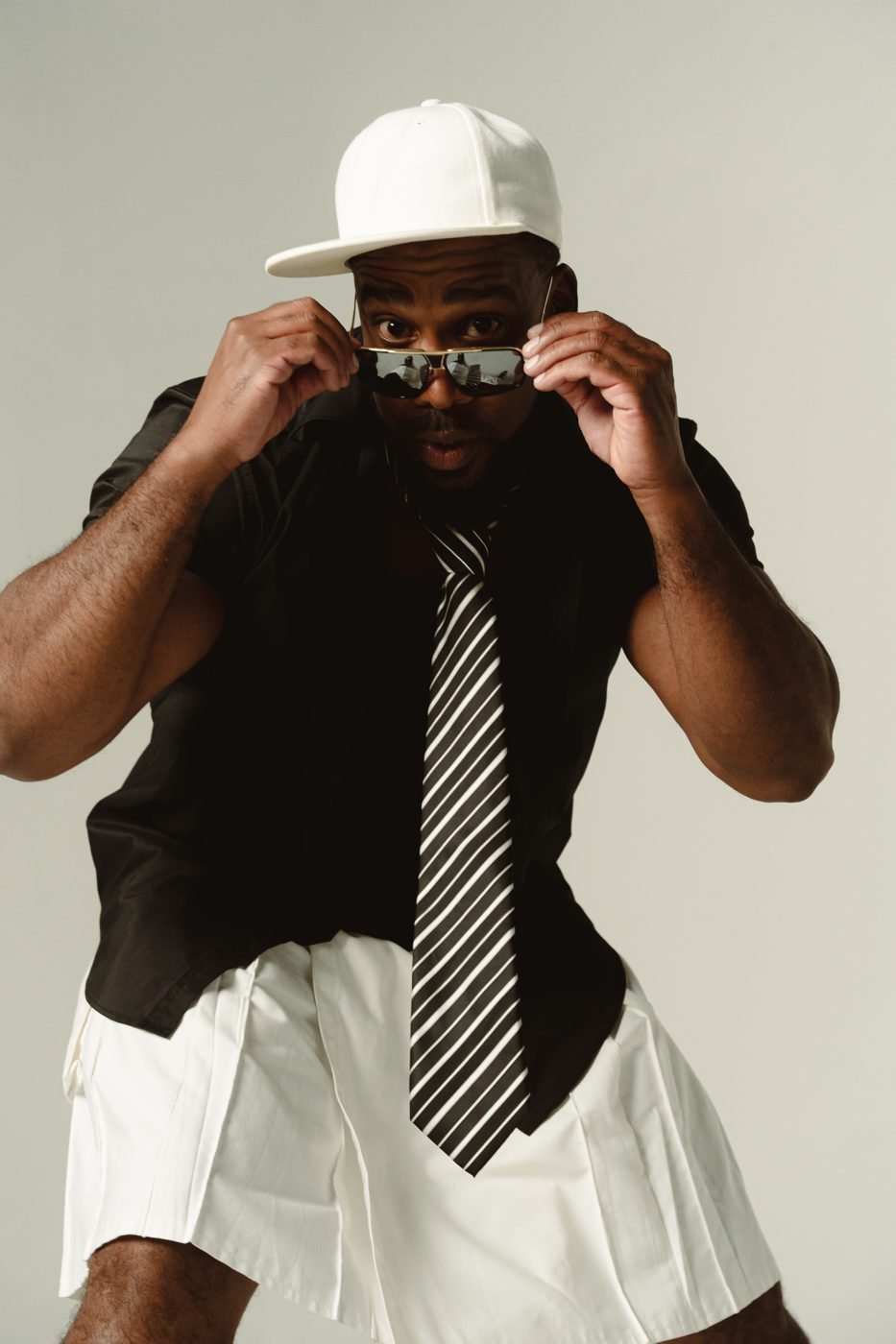 Bad Juju peering over his sunglasses in a white cap and striped tie